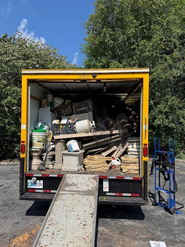 Box truck with its ramp down, loaded with tools, shelving and garage junk by Mitzvah Movers & Junk Removal