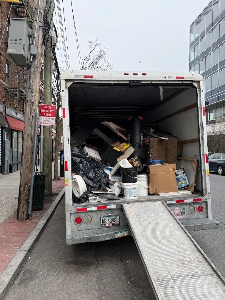 Box truck loaded with furniture and household junk, ramp down on a city sidewalk, ready for haul-away