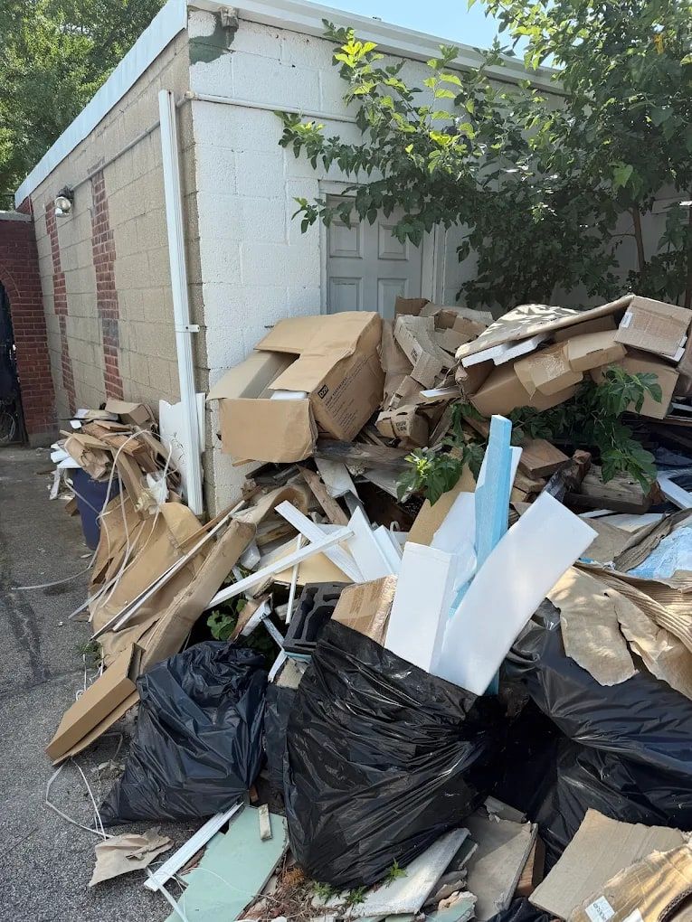 Pile of cardboard boxes, black bags and debris beside a garage, waiting for pickup
