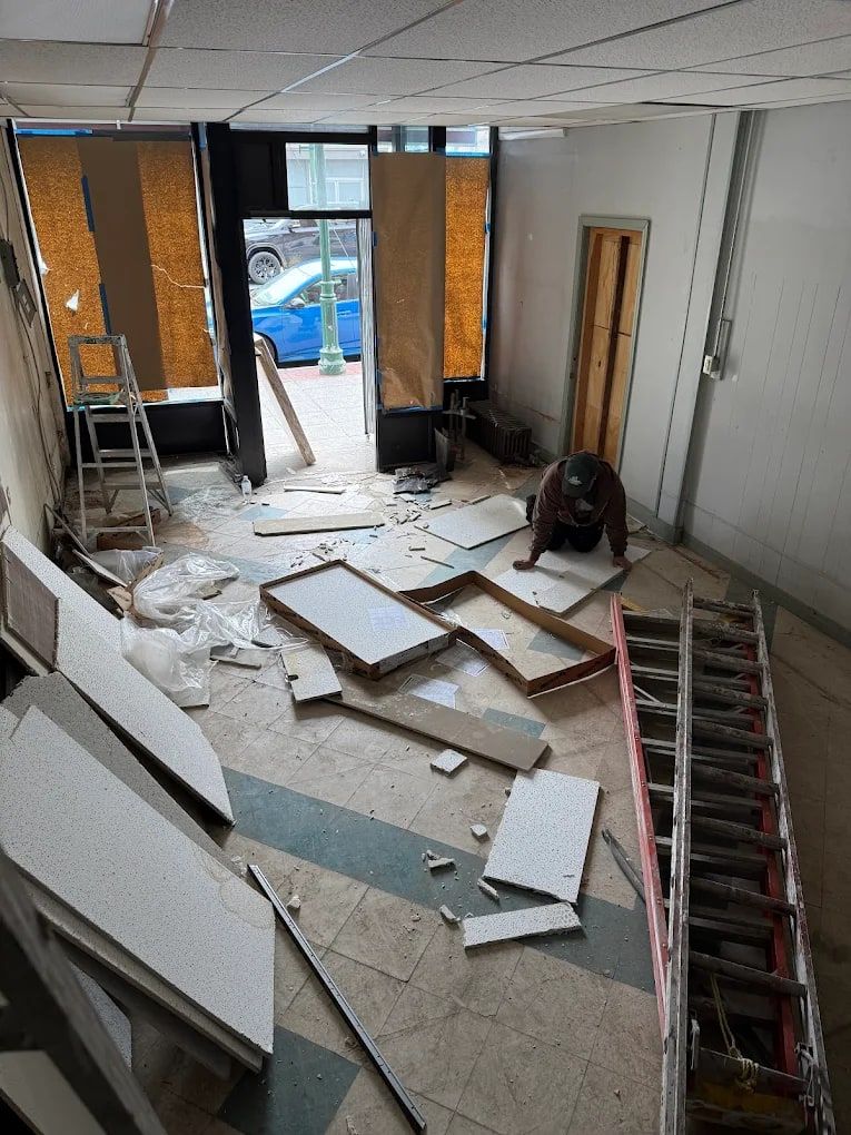 Commercial space with fallen ceiling tiles, broken drywall and a ladder, before renovation debris removal