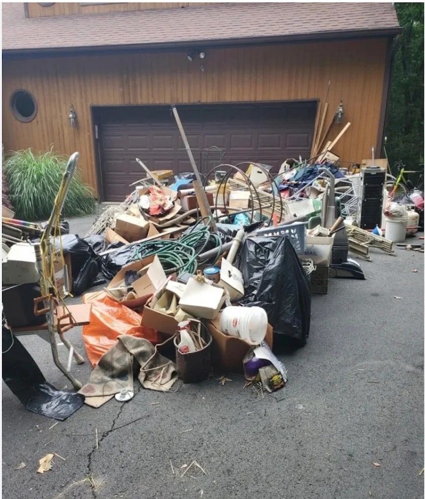 Large pile of junk, bags and boxes in a driveway in front of a garage during a cleanout