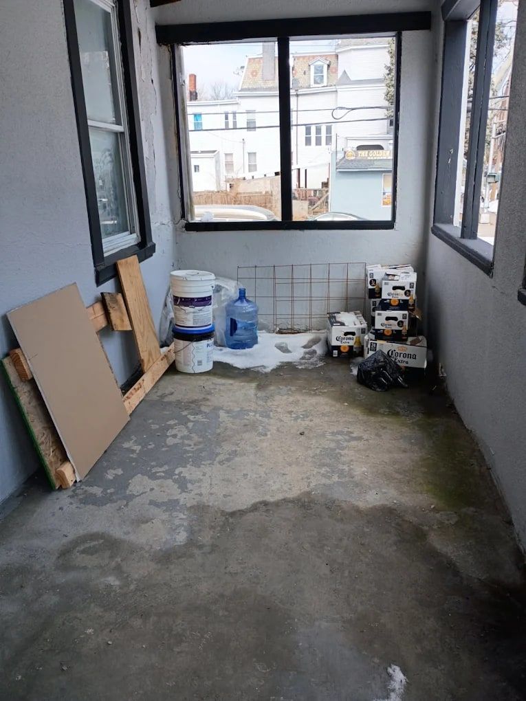 Empty enclosed porch with a bare concrete floor after a cleanout