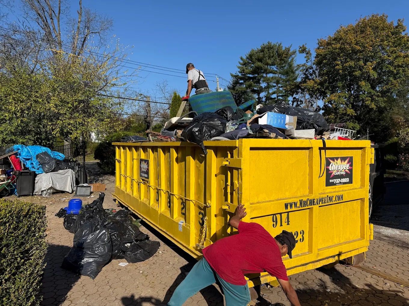 Crew member packing down a full dumpster of household items during a whole-house estate cleanout