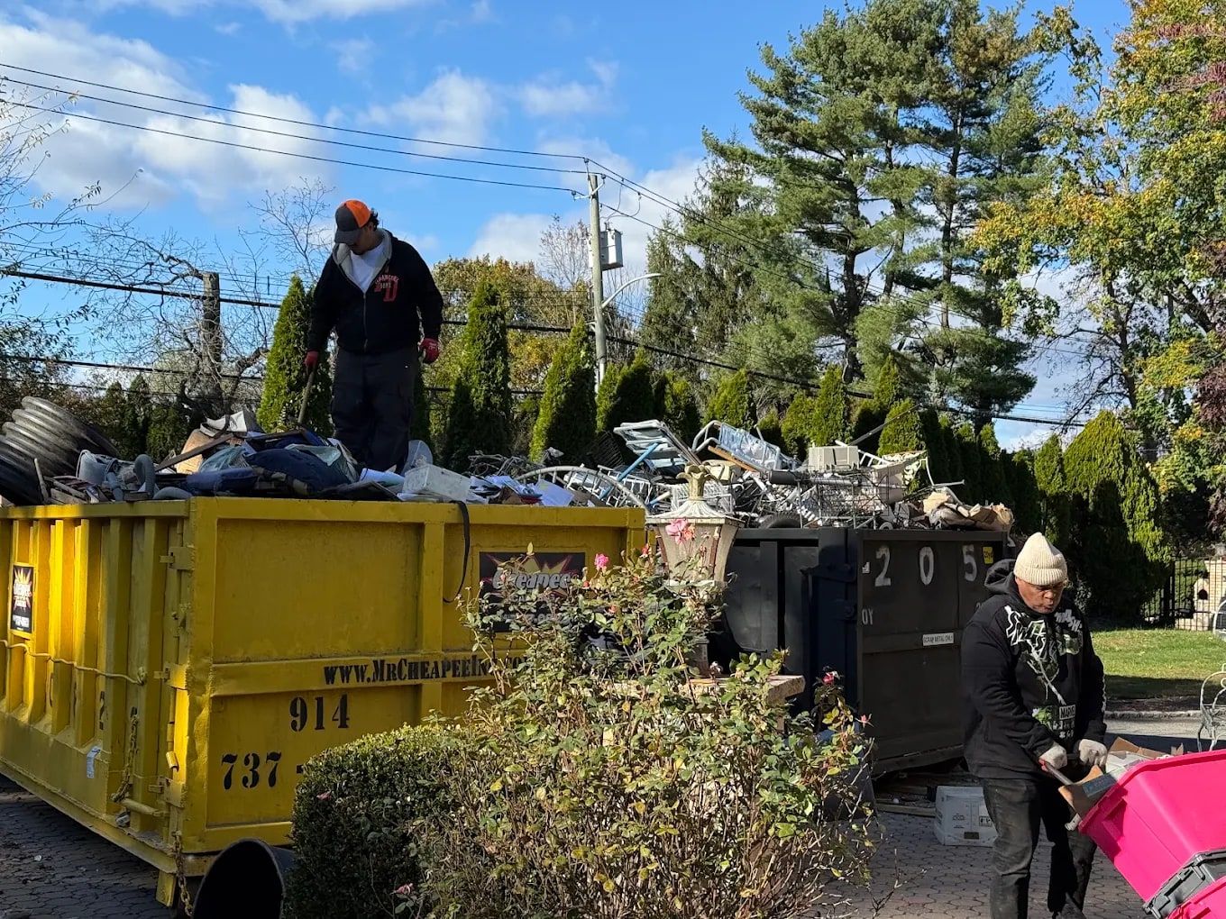 Estate cleanout crew loading furniture and household items into a roll-off dumpster outside a home