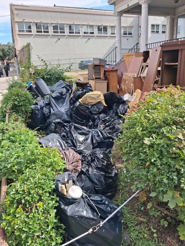 Black junk bags and old wooden furniture piled beside a building before haul-away