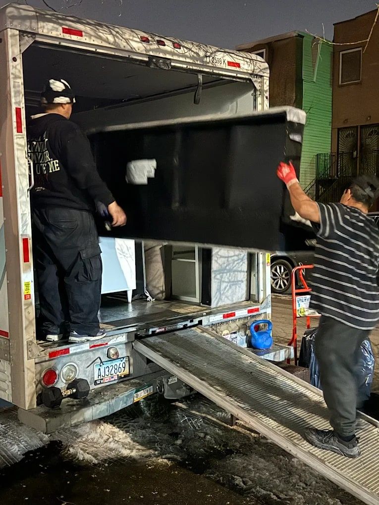 Two movers lifting a heavy black cabinet up the ramp into a box truck
