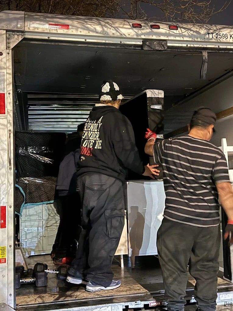 Two movers loading furniture into the back of a box truck from the ramp