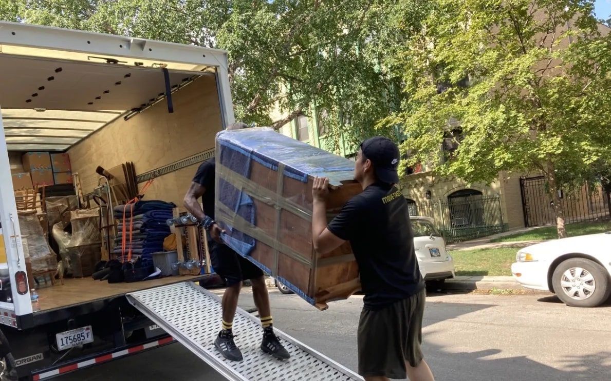 Mitzvah Movers crew carrying a blanket-wrapped dresser up the ramp into a moving truck