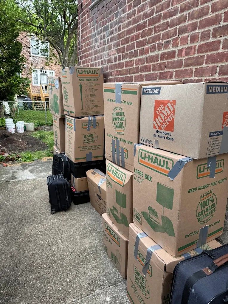 Packed and taped moving boxes and suitcases stacked outside a brick apartment building on moving day