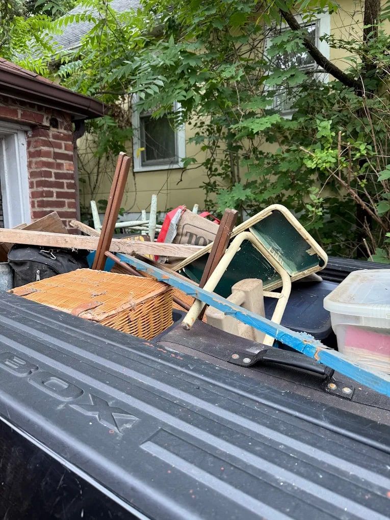 Pickup truck bed loaded with old chairs, a wicker basket and broken wood from a furniture haul-away
